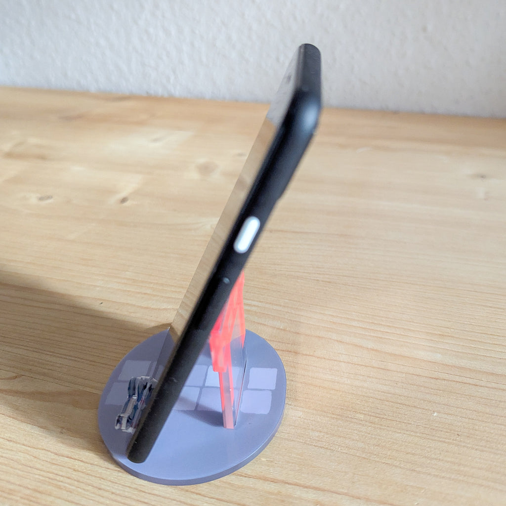 Schwarzes Smartphone auf dem roten Torii Smartphone-Ständer mit grauer Basis auf Holzuntergrund