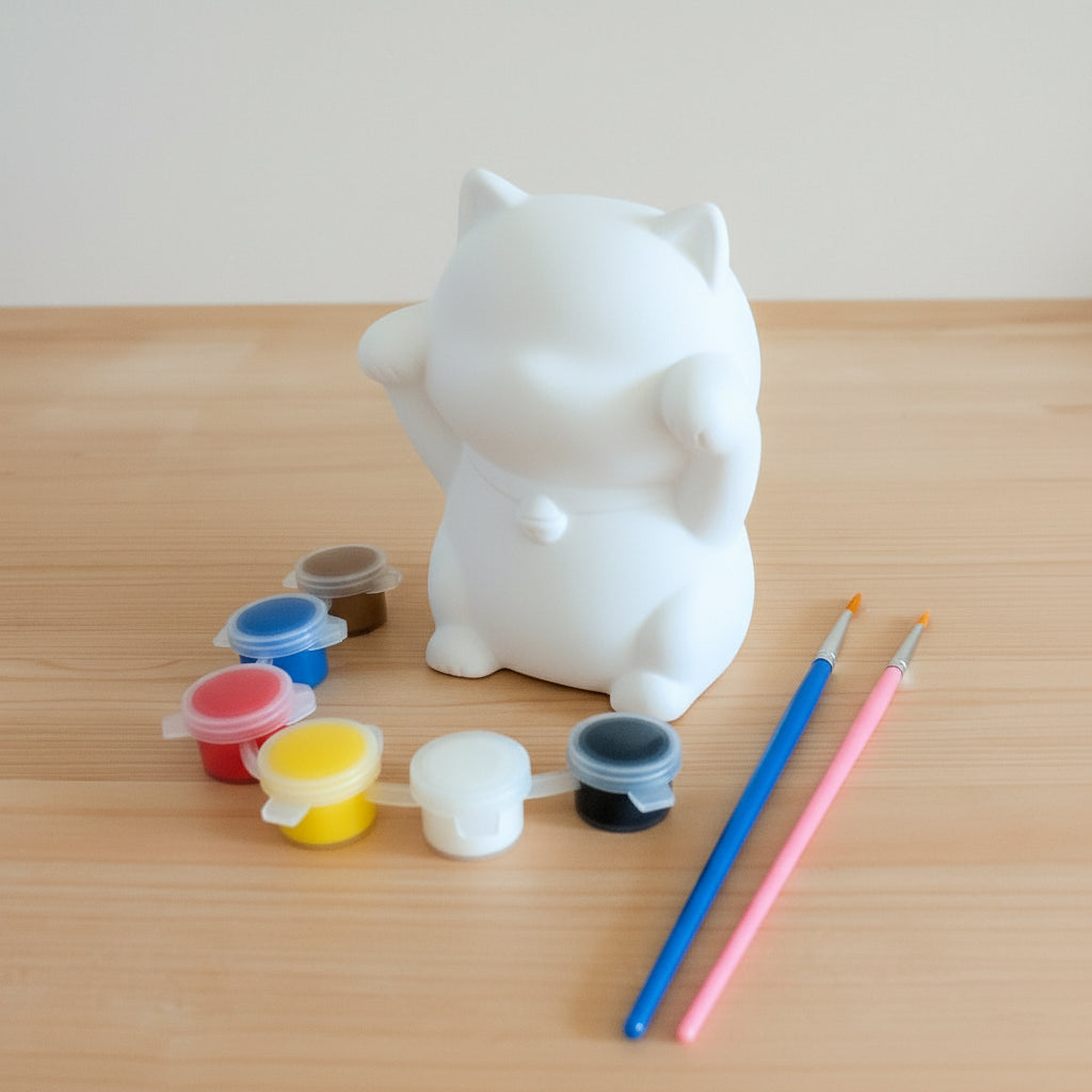 Nurie Mascot Bemalfigur Katze Set mit weißer Keramikkatze, sechs bunten Farbdosen und zwei Pinseln auf einem Holztisch