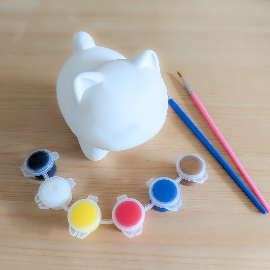 Weiße keramische Katzenfigur zum Bemalen mit farbigen Farbtöpfen und Pinsel