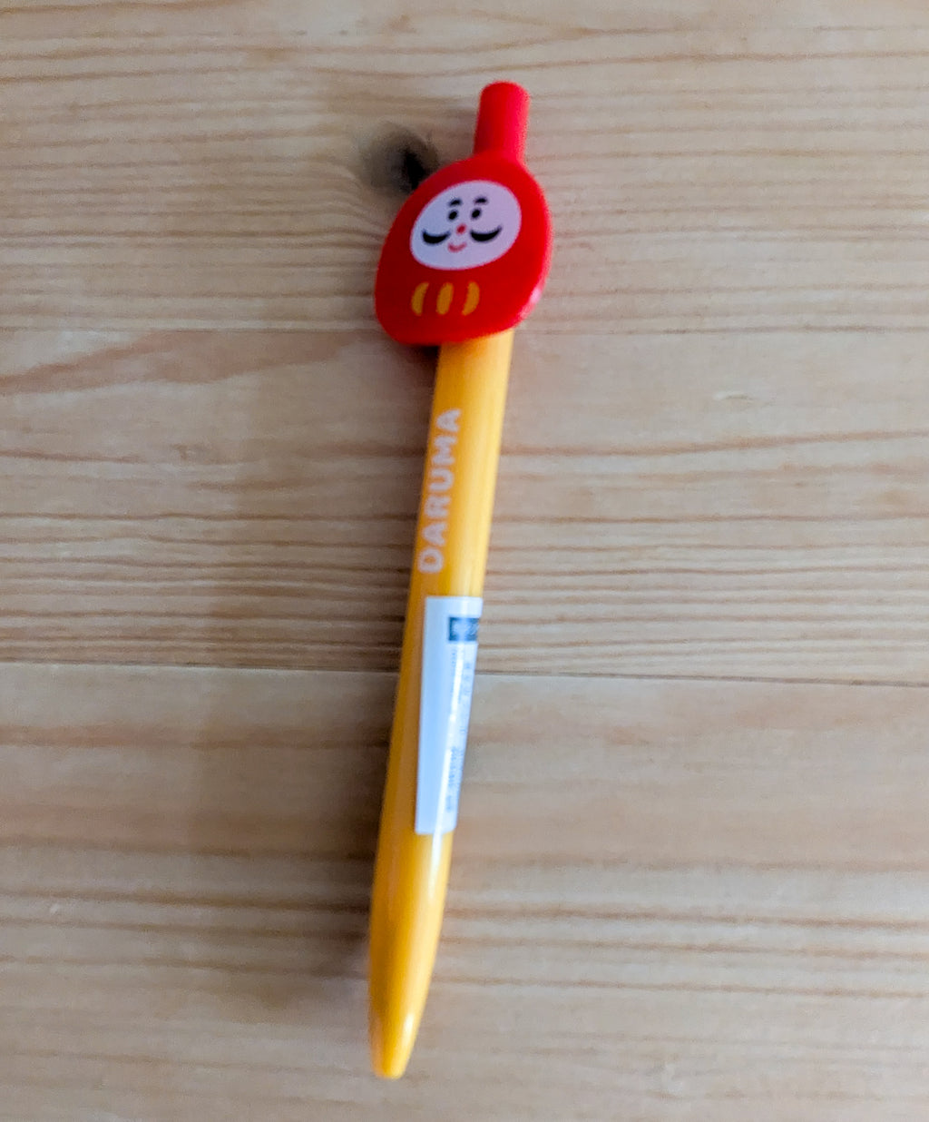 Daruma Kugelschreiber Nahaufnahme auf Holzhintergrund mit roter Glückspuppe und Tintenpatrone sichtbar