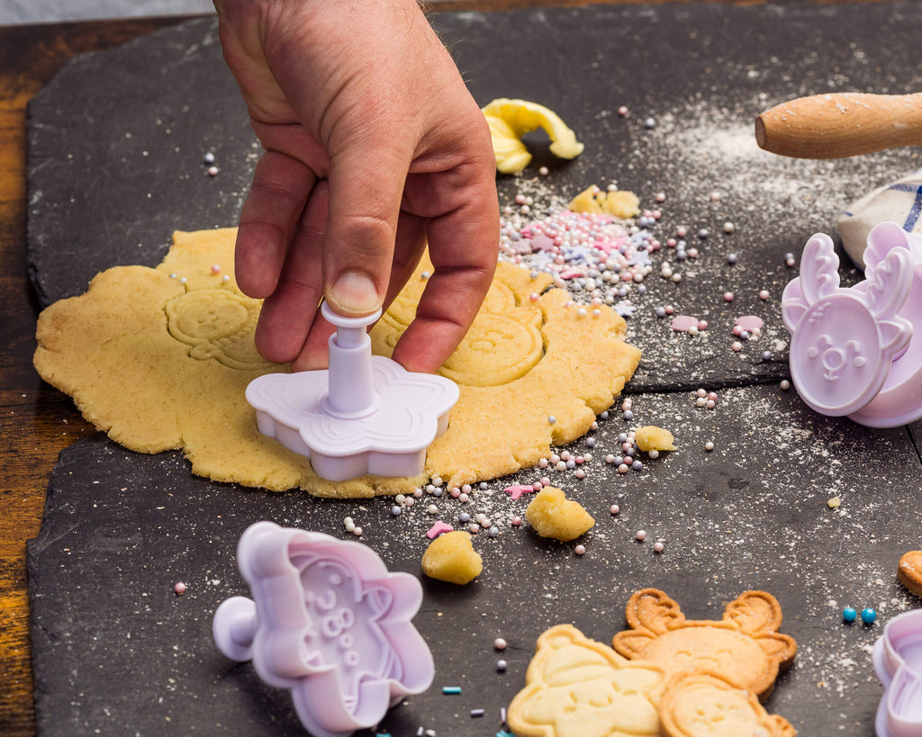 Weihnachtsbacken mit Snowchan Ausstechformen – Japanische Kawaii-Motive für Kekse. | Hand legt ausgestochenes Plätzchen auf Backpapier, fertige Kekse im Hintergrund.
